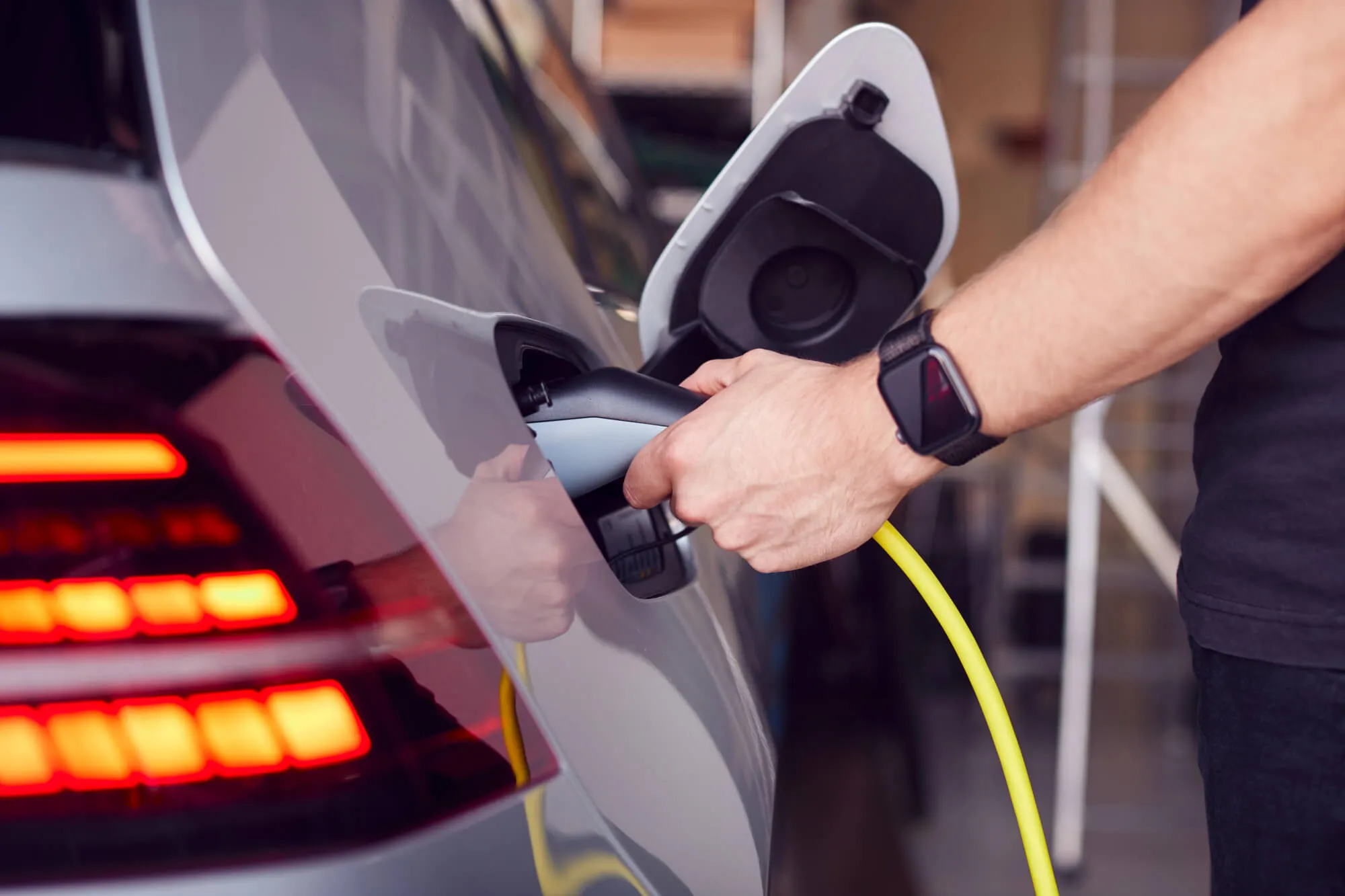 Man plugging a yellow charging cable into an electric vehicle — EV charging cost vs gas in North Carolina 2026